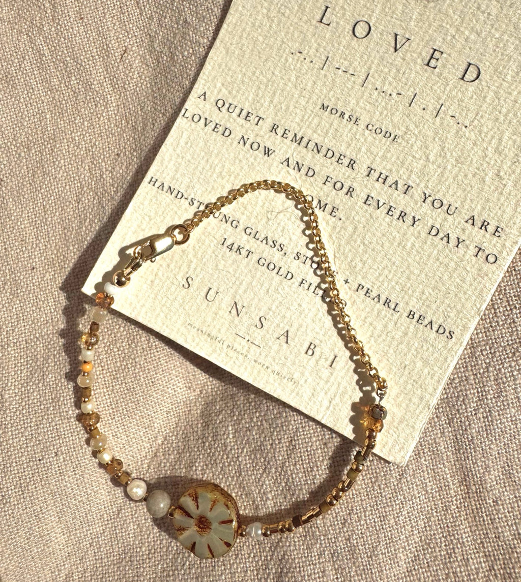 BLOOM bracelet with a SUNSABI LOVED Morse code story card on natural linen.