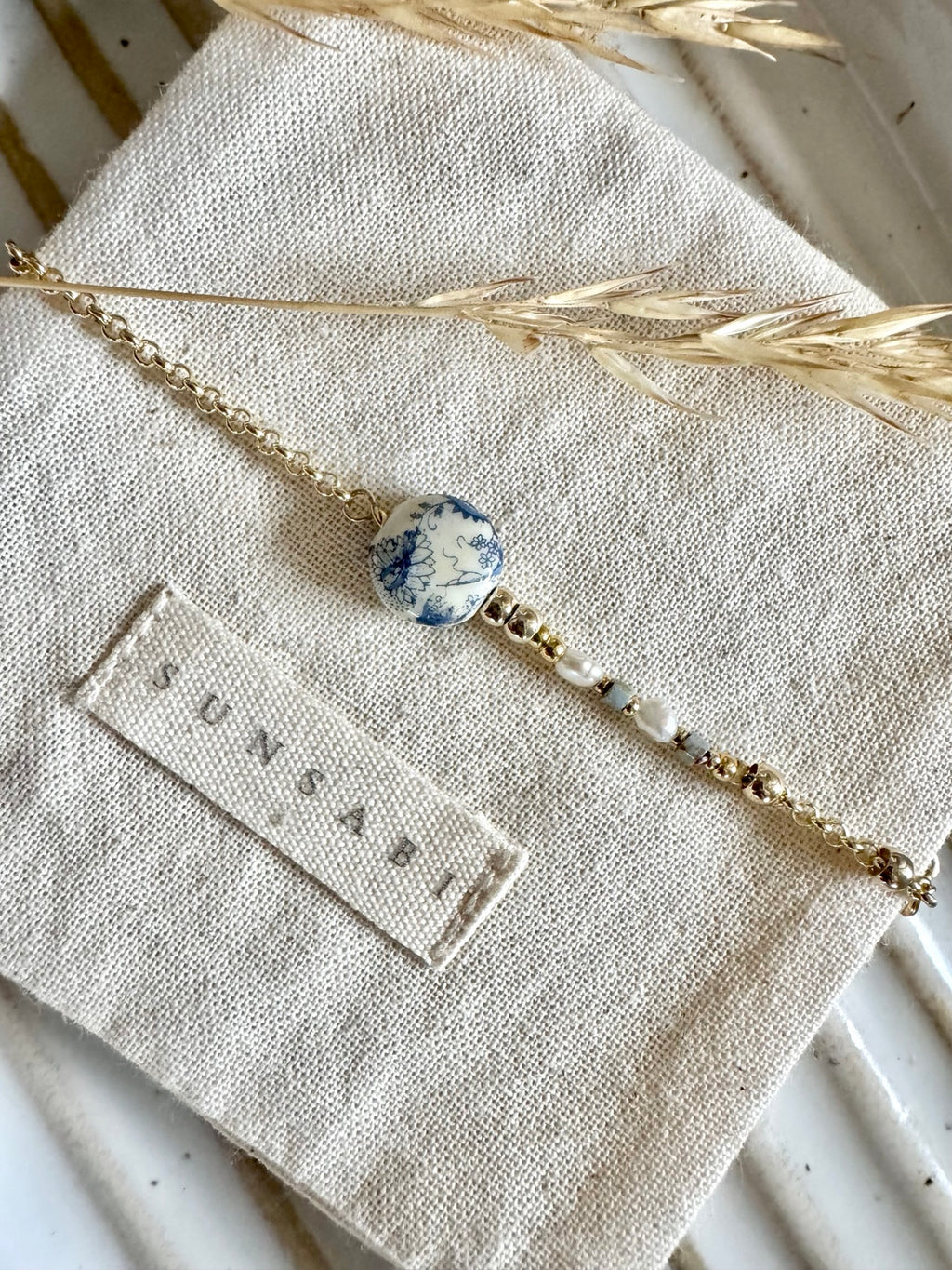 SUNSABI Portobello Sky bracelet displayed on natural linen with a vintage blue floral Japanese Tensha bead and 14k gold-filled details