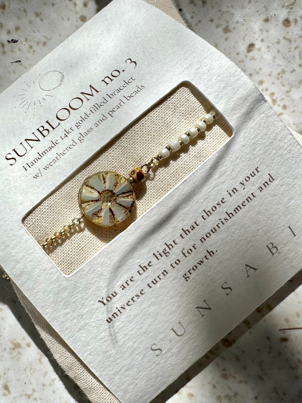 Angled view of SUN BLOOM No. 03 with ivory glass beads and a weathered Czech bloom in its story packaging